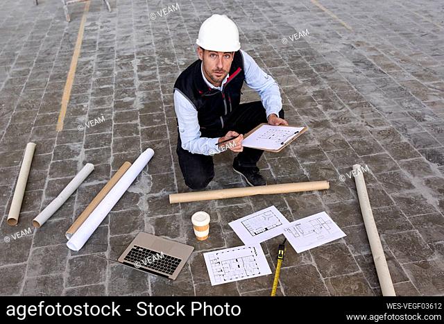 Male engineer holding site plan while kneeling on floor in building