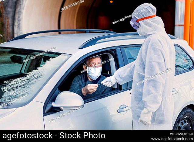 Man wearing protective clothing controlling senior man in car