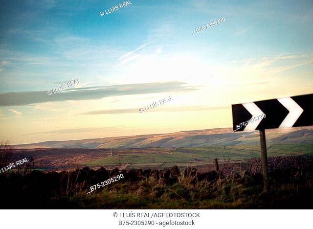 North Yorkshire landscape at sunset, with a traffic sign in the foreground with directional arrows to the right. North Yorkshire, England, UK