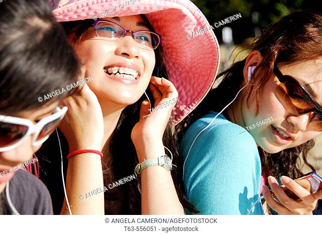 3 asian women sitting together on beach listening to music