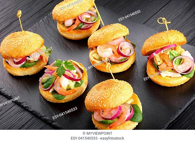 delicious small burgers pinned with bamboo skewers or pinchos with shrimps, calamari, mussels, red onion rings and finely chopped cucumber on slate tray