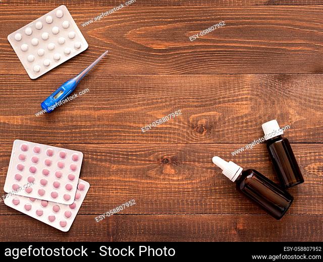 medications or tablets and drops and electronic thermometer on a dark wooden background with copy space. Flat lay or top view