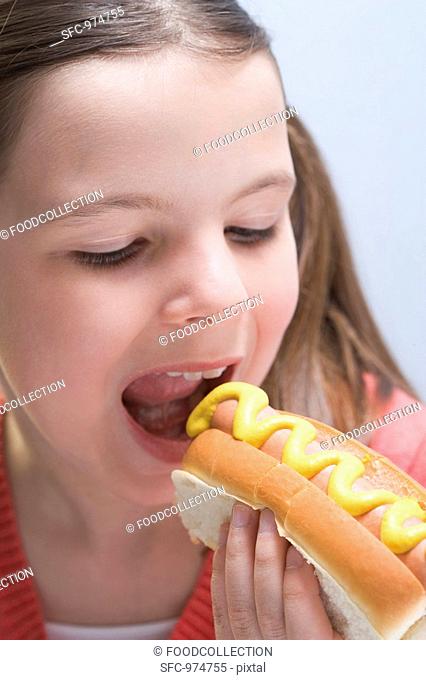 Girl biting into a hot dog with mustard