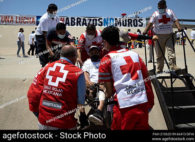 19 June 2021, Mexico, Ciudad Juarez: Red Cross workers help a man at the border wall between Mexico and the US during the ""#HugsNotWalls"" action of the NGO...