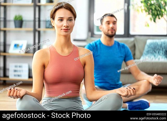 happy couple meditating in yoga lotus pose at home