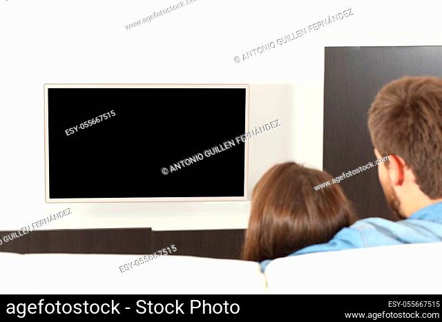 Back view of a couple cuddling watching tv with blank screen sitting in the sofa at home