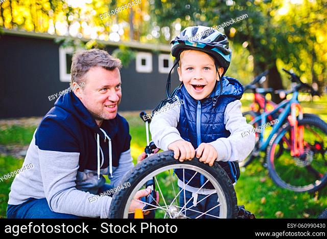 Father's day Caucasian dad and 5 year old son in the backyard near the house on the green grass on the lawn repairing a bicycle, pumping a bicycle wheel