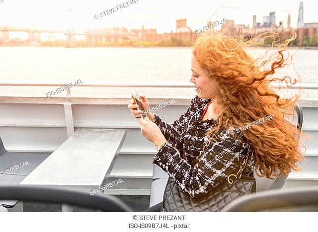 Young businesswoman on passenger ferry deck looking at smartphone