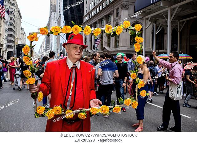 New York, NY - April 16, 2017. A man in red carries a large frame covered in orange flowers as if he were a painting at New York's annual Easter Bonnet Parade...