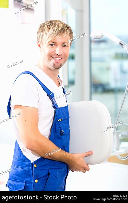 Portrait of a cheerful man wearing blue overall while working in a sanitary ware shop with modern fixtures and accessories for sale