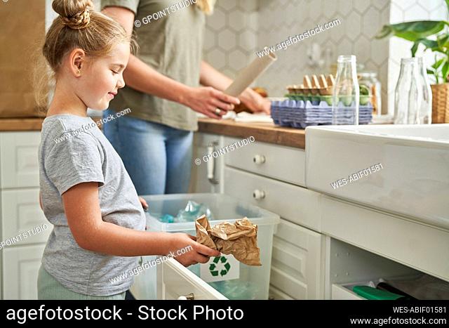 Girl collecting garbage in recycling bin at home