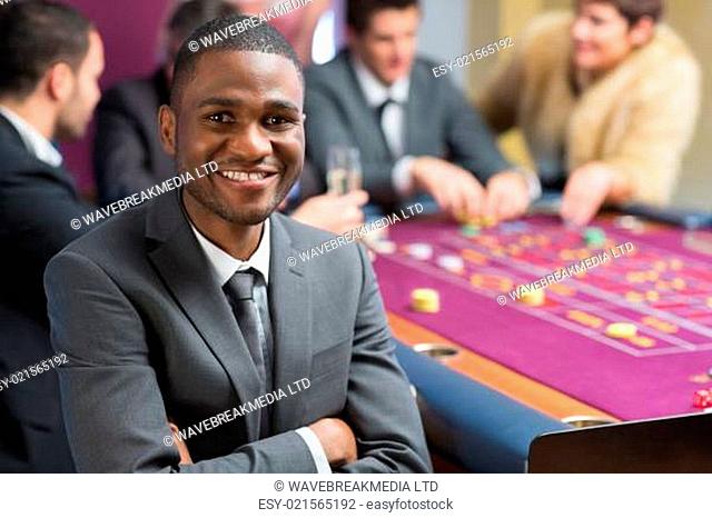 Smiling man sitting at the casino arms crossed at roulette table