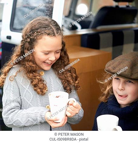 Girls drinking hot chocolate beside camper van