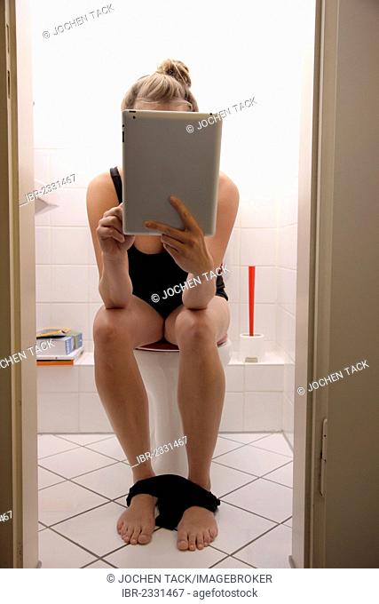 Young woman on the toilet surfing with an iPad, tablet computer in the internet via wireless connection