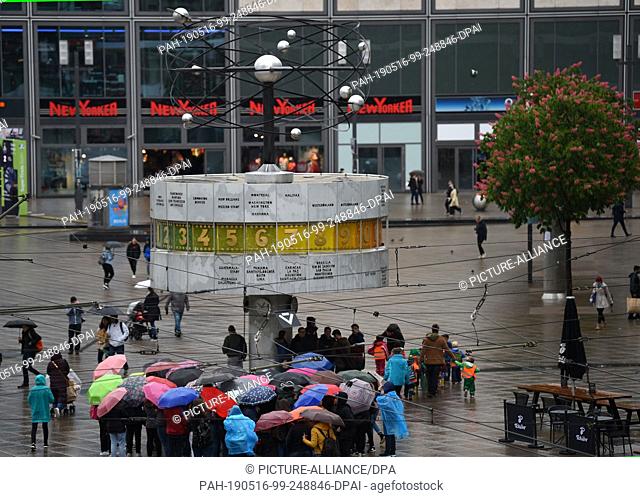 16 May 2019, Berlin: A group with umbrellas stands at the world time clock on Alexanderplatz in Berlin-Mitte. Photo: Sven Braun/dpa