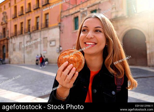 Street food in Murcia, Spain. Beautiful tourist girl holding pastel de carne murciano (Murcian meatloaf) in Murcia street, Spain