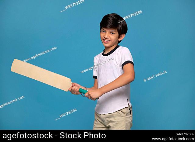Portrait of a boy batsman ready to face the ball against blue background