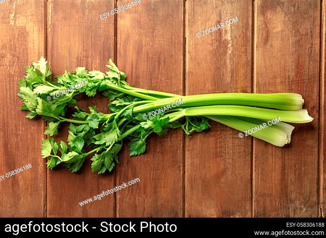 A photo of fresh organic celery leaves and stalks, shot from the top on a dark rustic wooden background