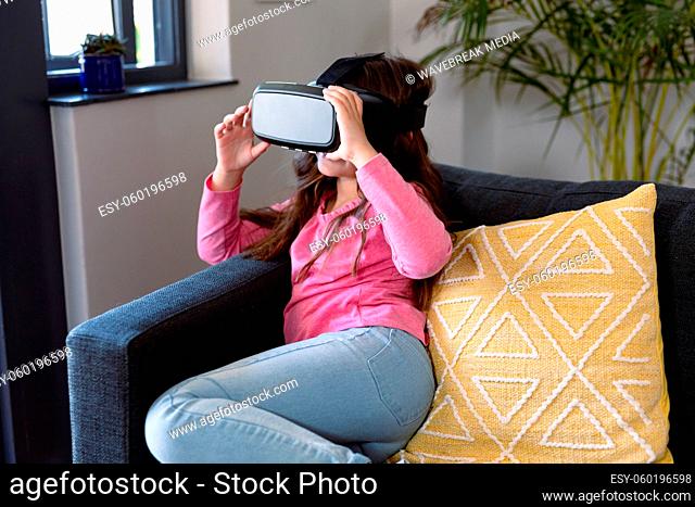 Happy caucasian girl sitting on sofa, wearing vr headset, having fun