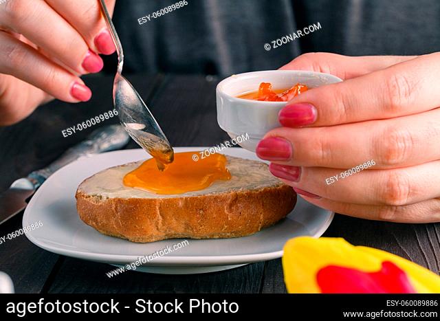 Breakfast concept. Woman take jam on buttering bread with tulips on table