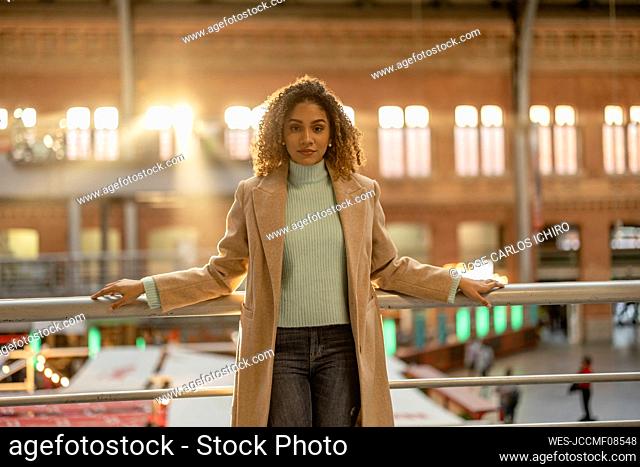 Confident young beautiful woman with curly hair in front of railing