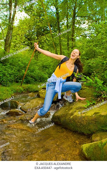 Young woman hiking through the woods and trying to cross a stream and accidentally falling into the water
