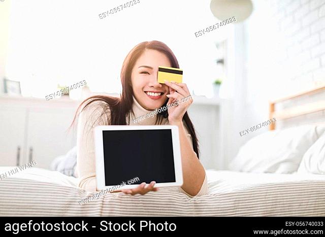 Smiling young woman showing credit card and using tablet to shop online at home