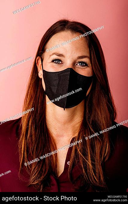 Young businesswoman wearing FFP2 face mask standing against colored background
