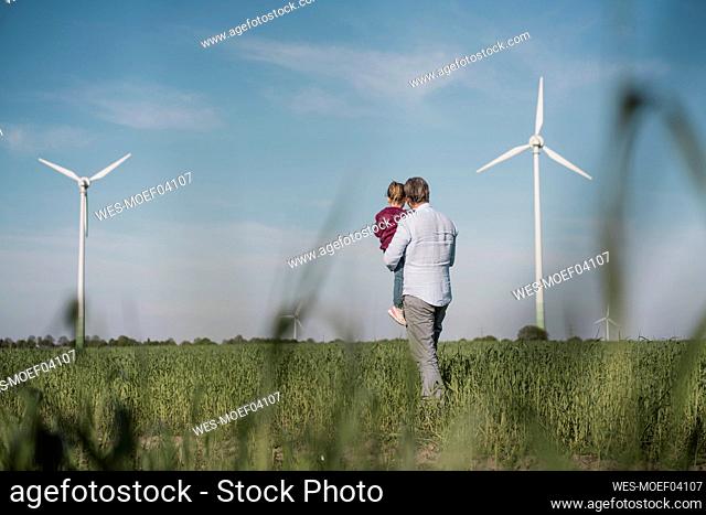 Man carrying daughter standing in field on sunny day