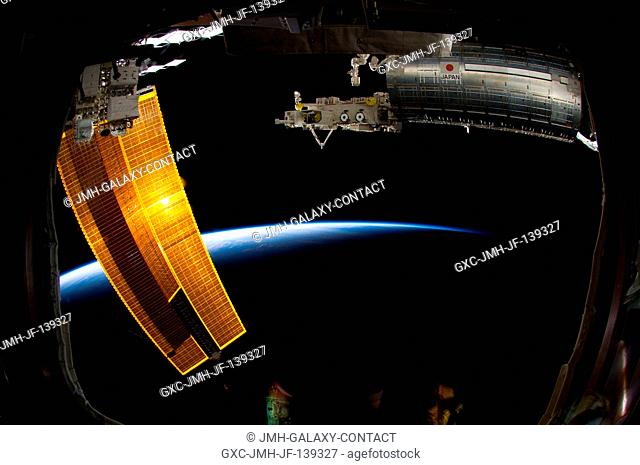 Backdropped by the thin line of Earth's atmosphere and the blackness of space, the Japanese Kibo complex of the International Space Station and station solar...