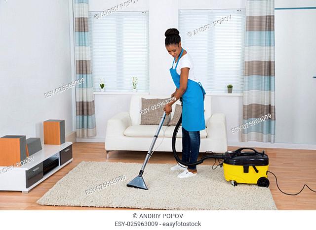 Young African Woman Cleaning Carpet With Vacuum Cleaner