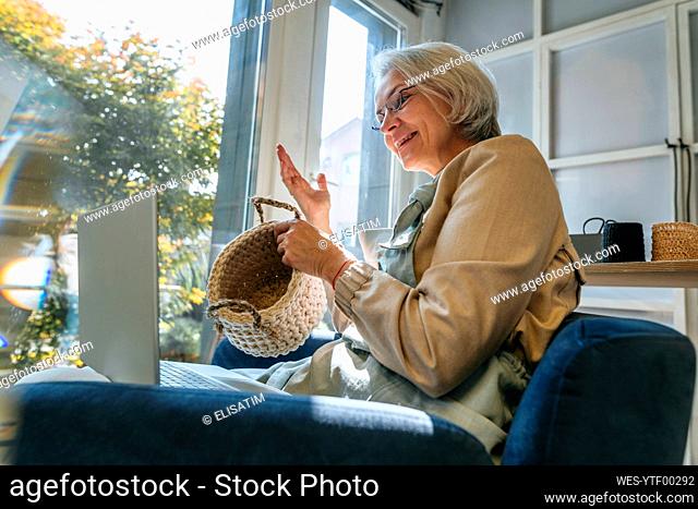 Happy craftswoman showing crochet basket on video call through laptop in workshop