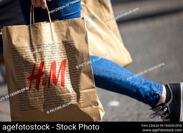 PRODUCTION - 24 June 2023, North Rhine-Westphalia, Cologne: A woman carries a paper bag with the logo of the department store chain H&M in Cologne's...