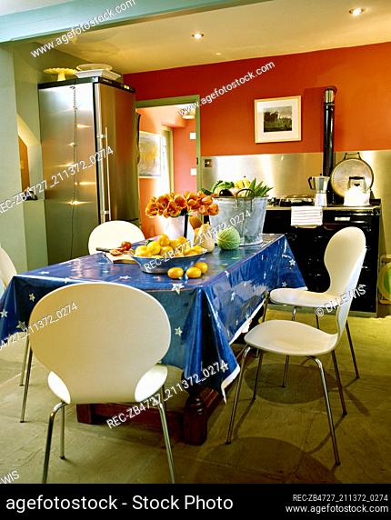 Table with blue tablecloth and moulded plastic chairs in kitchen with aga