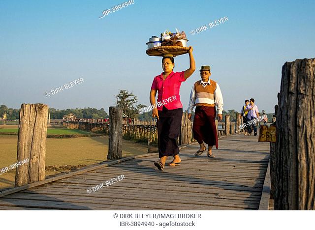 Woman with tanaka on her face carrying food on her head on a teak bridge, U Bein Bridge, over Thaungthaman Lake, Amarapura, Mandalay Division, Myanmar