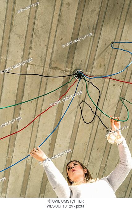 Young businesswoman in office examining cables at light bulb