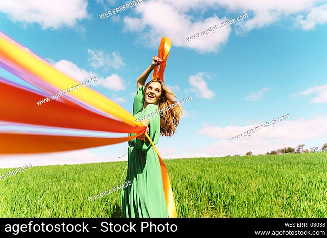 Happy young woman wearing a green dress in a field with blowing ribbons