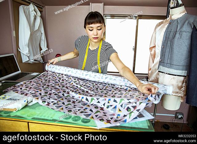 Japanese female fashion designer working in her studio, measuring fabric