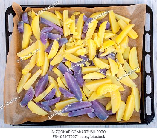 Raw peeled and sliced blue and yellow potatoes, on on a baking sheet
