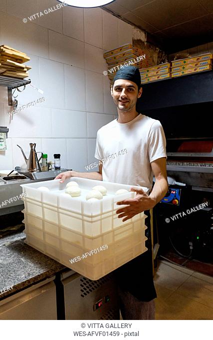 Portrait of smiling pizza baker with boxes of dough in kitchen