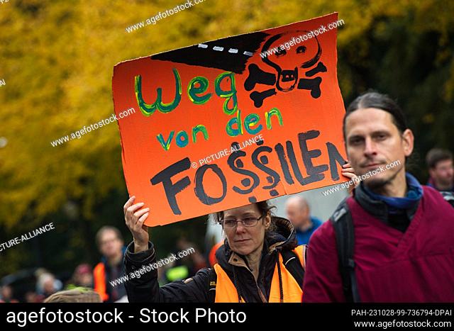 28 October 2023, Berlin: An activist holds a placard reading ""Away from fossils"" while environmental activists occupied the street of June 17