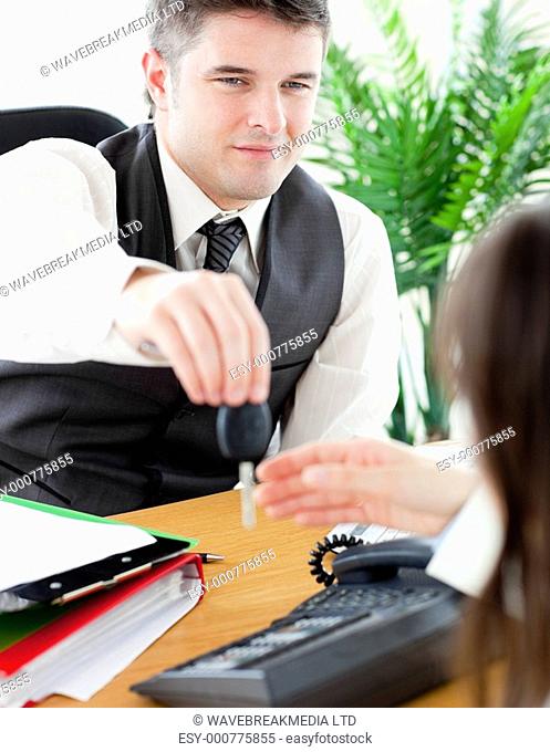 Charming salesman giving cars key to his customer sitting in his office