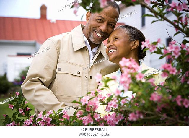 Close-up of a senior man and a senior woman smiling behind flowers