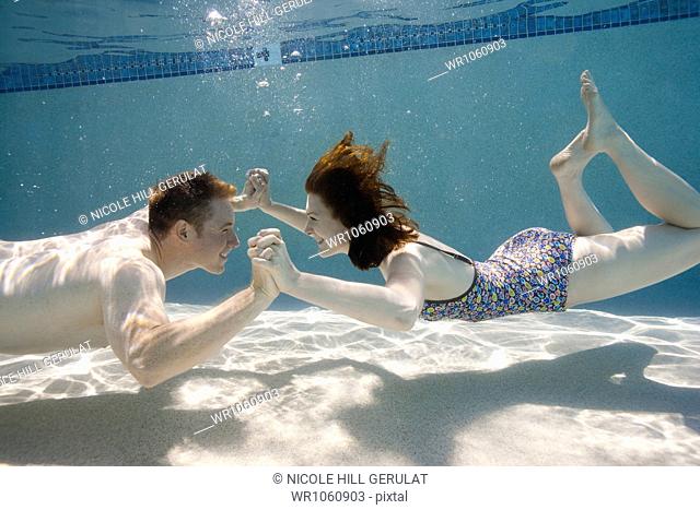 USA, Utah, Orem, Happy young couple holding hands in swimming pool
