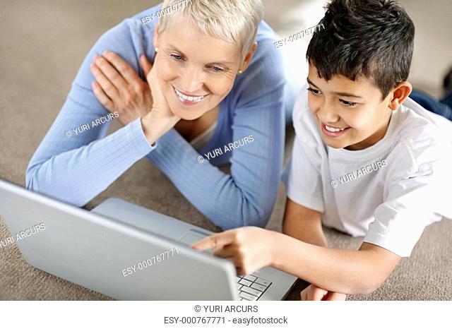 Closeup of a grandson showing something to smiling grandmom on a laptop