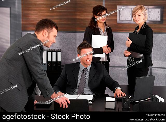 Businesspeople working at desk, boss sitting at desk, colleagues looking at laptop computer screen