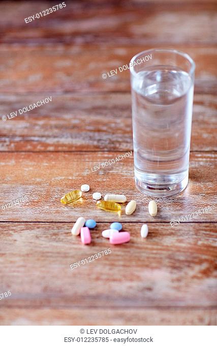 medicine, nutritional supplements and food additives concept - - close up of vitamin pills with cod liver oil capsules and water glass on table