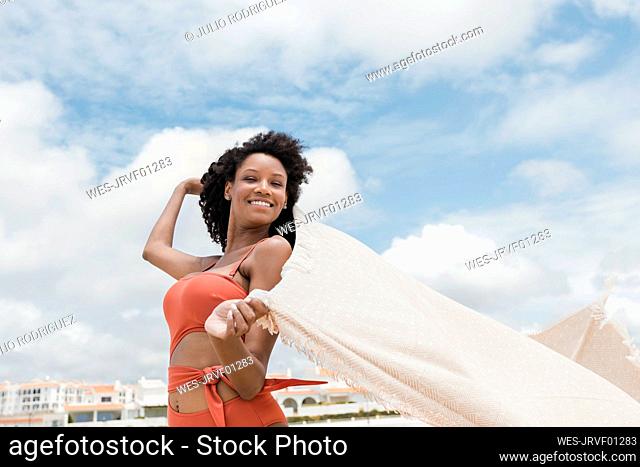 Smiling beautiful young woman holding beach towel on sunny day