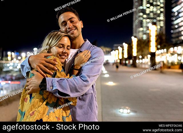 Smiling young couple with eyes closed embracing each other at night