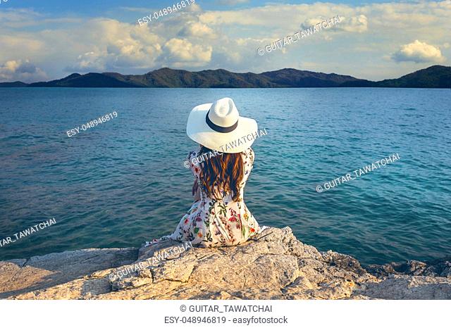 Young woman sitting on the top of rock and looking at the seashore. Vintage tone